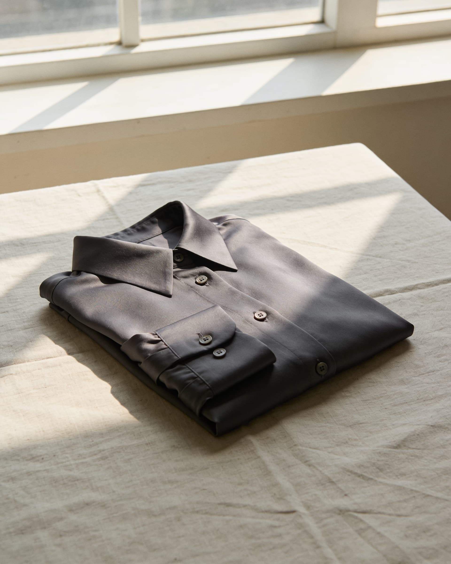 Puño y cuello de la blusa de seda charcoal, doblada sobre lino crudo