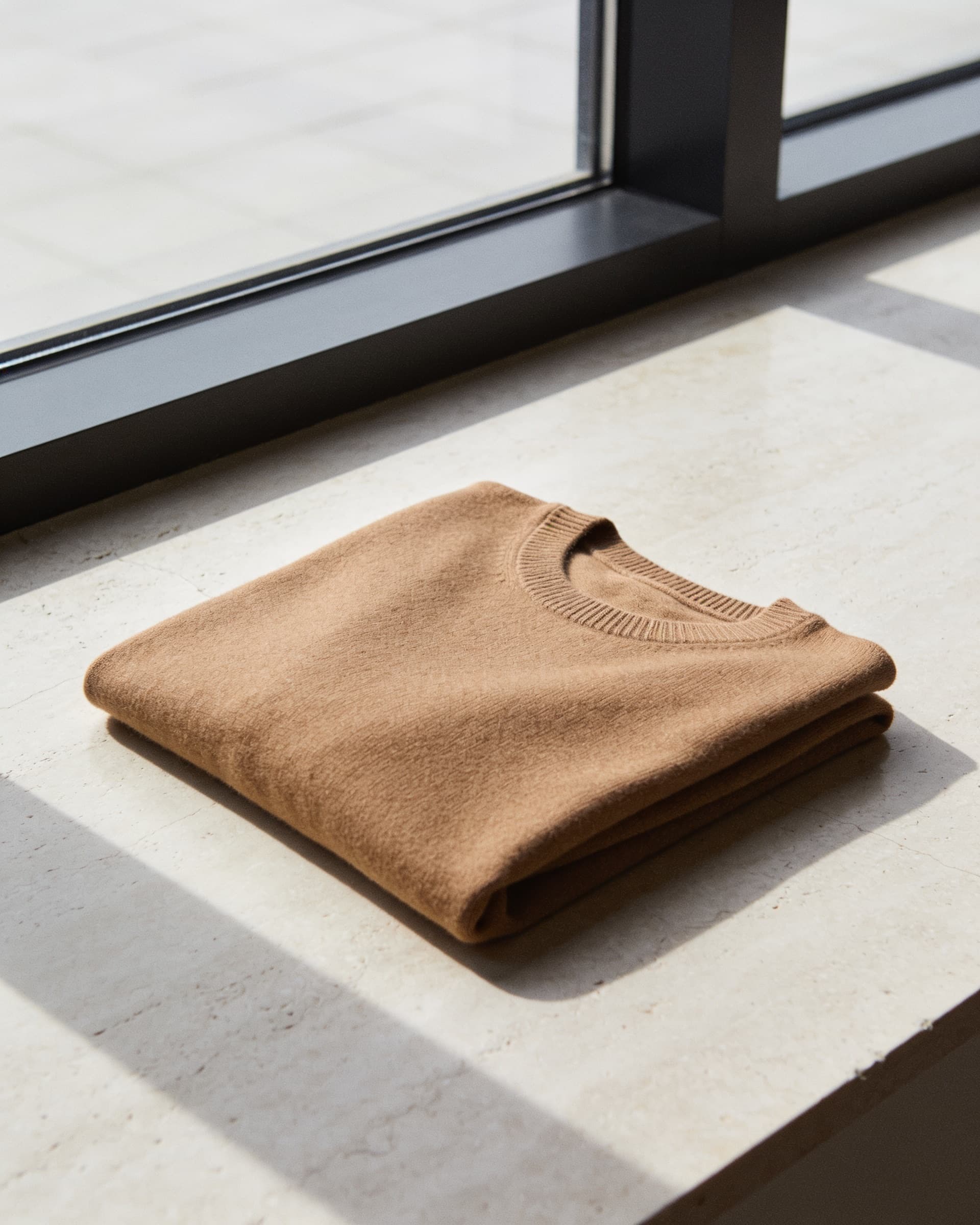Suéter de merino camel doblado sobre piedra, con la trama del punto visible