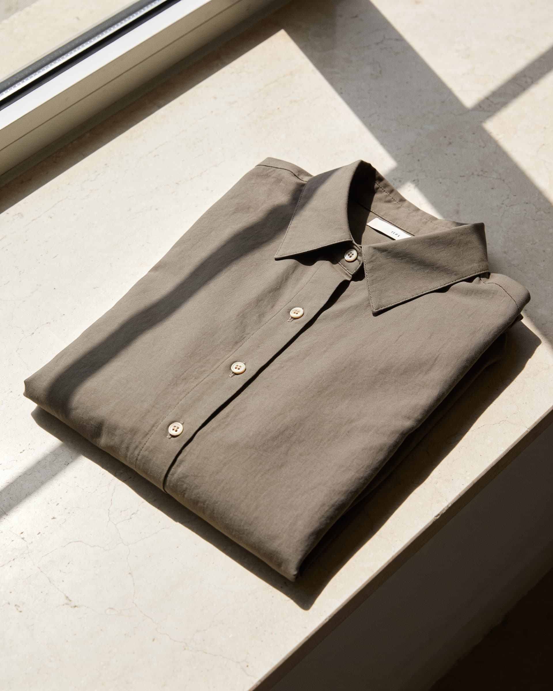 Cuello y botonadura del vestido camisero taupe, doblado sobre piedra